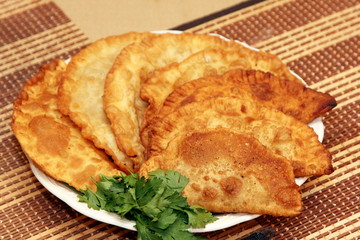 Chebureki or fried pie with beef meat on plate decorated with green parsley on bamboo mat background