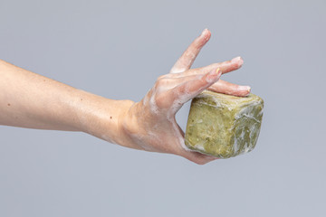 White people's hands washing each other with green foamy 
Marseille's soap isolated in front of a grey background with structurant lights and shadows