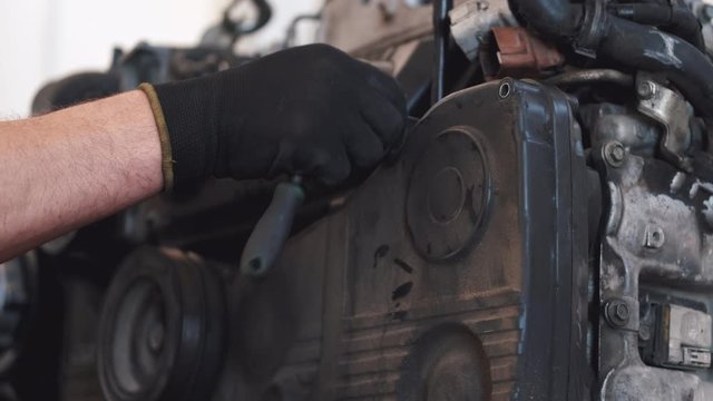 Person repairs engine in garage. He wears black gloves. Man uses tools.