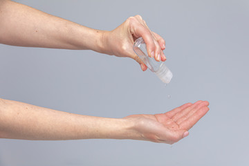 White people's hands using alcohol sanitizer isolated in front of a grey background with structurant lights and shadows