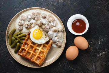 Belgian potato waffle with champignons, fried egg and pickles over dark brown stone background, flatlay, horizontal shot