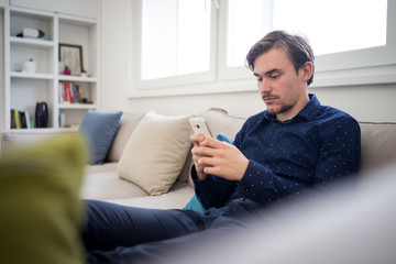 Young attractive man on sofa with smartphone