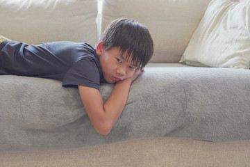 Mixed race Asian preteen boy feeling bored lying on sofa at home, social distancing, quarantine, isolation concept, autism awareness, mental health