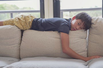 Mixed race Asian preteen boy feeling bored lying on sofa at home, social distancing, quarantine,...