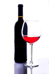   A thin-stemmed glass of red wine and a bottle of wine.