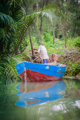 Obraz premium Vietnamese man in a boat tending to vegetation on the river bank.