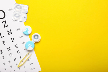 Containers with contact lenses, tweezers and eye test chart on color background