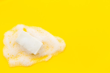 Soap bar with foam on yellow background top-down copy space