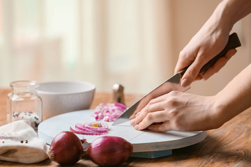Obraz na płótnie Canvas Woman cutting fresh raw onion in kitchen, closeup