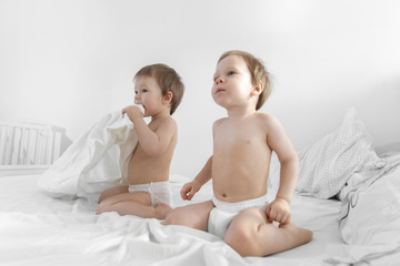 Small twins sit and play on bed. Babies twins sit down in Bed. Fashion image of baby and family