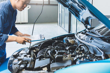 Asian Man mechanic inspection writing note on clipboard.Blue car for service maintenance insurance...