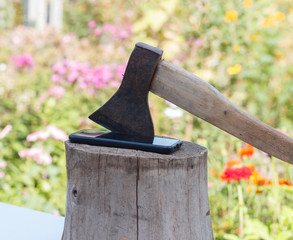 an axe is stuck in a wooden stump on a stand, next to an iPhone