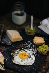 Fried egg with parmesan and toast with cream cheese and avocado paste on black plate, top view