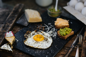 Fried egg with parmesan and toast with cream cheese and avocado paste on black plate, top view