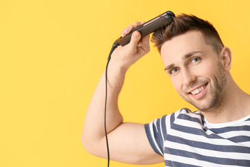 Handsome young man with flattening iron on color background