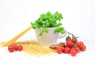 close up of spaghetti, tomatoes and a cup with basil on the white background