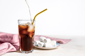 Pouring of milk into cold coffee in glass on light background