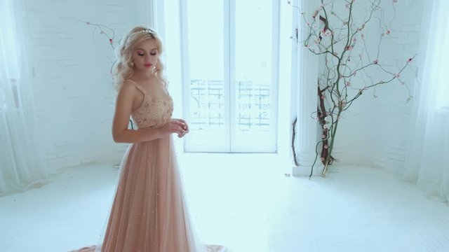 Princess lady sad. backdrop white classic home room interior kids colored toys. Delicate beige evening long luxury sexy dress train. Queen woman hairstyle loose wavy blonde hair. Tiara earrings pearls