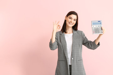 Young woman with calculator showing OK on color background