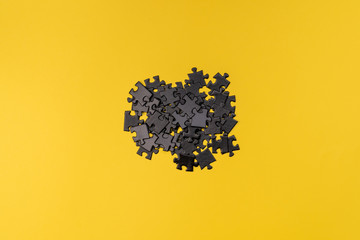 A handful of black puzzles in the center of the frame on a yellow background