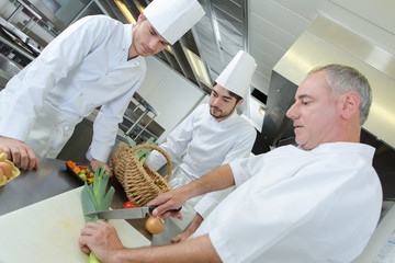 restaurant worker and apprentices cutting fresh pepper for salad