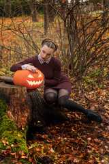   Halloween Witch with a carved Pumpkin in a autumn forest. Beautiful young woman in witches dress costume holding pumpkin.  Halloween party