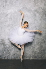 Pretty young ballerina dancer dancing classical ballet against rustic wall