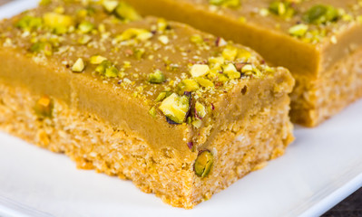 Slices of baked Ginger Crunch covered with Pistachios, Rolled Oats, Ground Ginger on a white plate
