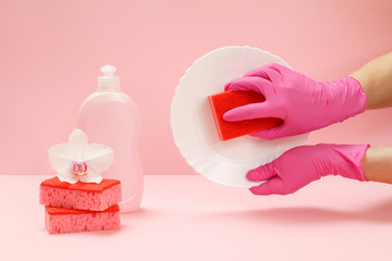 Women's hands in latex gloves with a sponge and a plate on the pink background.