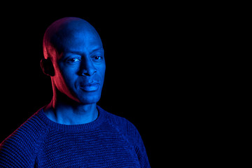 Black man with blue and red light, isolated on black background, looking at the camera. Copyspace.