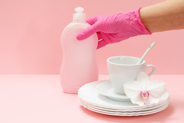 Woman's hand in protective glove with bottle of dishwashing liquid on a pink background.