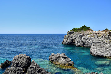 Fototapeta na wymiar Paleokastritsa / Corfu, Greece - Gray rocks in the blue-turquoise water of the Ionian Sea near Limni Beach, blue sky, in the summer during the daytime.