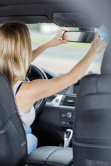 young woman driver adjusting her rearview mirror in the car