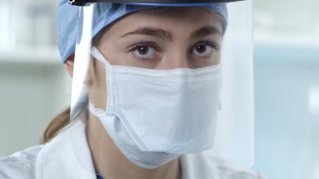 Female nurse working in lab looking up with face mask and shield covering her face.
