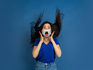 Shocked. Portrait of young caucasian woman with emotion on her protective face mask isolated on studio background. Beautiful female model. Human emotions, facial expression, sales, ad concept.