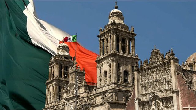 photomontage of mexico city cathedral over mexican flag in the wind, blue sky background,slow motion