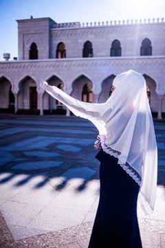 Bright shot a girl in a white shawl moves against the background of an urban gray beautiful mosque