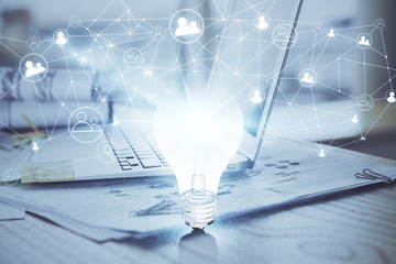 Computer on desktop in office with bulb icon hologram. Multi exposure. Concept of idea.
