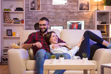 Cheerful young couple laughing while watching a tv show