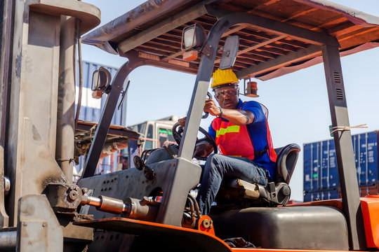 Worker man in hardhat and safety vest sitting in container stackers control loading containers box from cargo