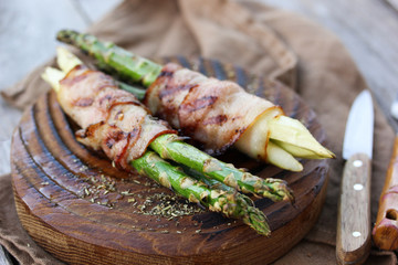 Grilled dishes. Asparagus with bacon on a wooden board with spices and salt. Grilled vegetables. Knife and fork. Background image, copy space