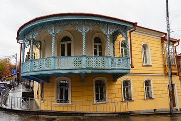 Fototapeta na wymiar Sololaki area with old vintage houses. Blue wooden round ornamental balcony on a yellow small house. Raining, autumn.