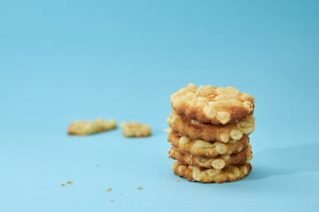 Pieces of broken biscuits on the left from cheese cookies, placed on top of each other, like a pyramid, isolated on light blue background. Nutritious snack.