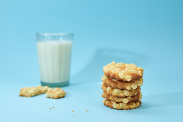 Cheese cookies are placed on top of each other, like a pyramid, with glass of white milk or yoghurt isolated on light blue background. Nutritious snack for lunch.