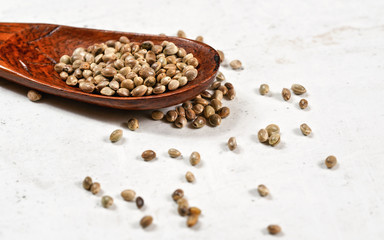 Unpeeled hemp - Cannabis sativa - in small dark wooden spoon on white stone board desk