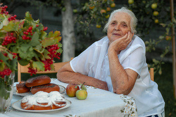 horizontal closeup portrait of a ninety year old gray-haired woman sitting at a table in her garden