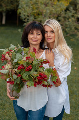 vertical close-up portrait of a fifty-year-old woman with a bouquet of viburnum in the arms that her thirty-year-old daughter hugs