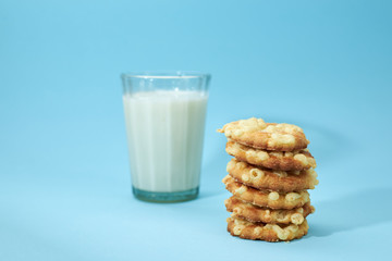 Cheese cookies are placed on top of each other, like a pyramid, with glass of white milk or yoghurt isolated on light blue background. Nutritious snack for lunch.