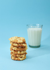 Cheese cookies are placed on top of each other, like a pyramid, with glass of white milk or yoghurt isolated on light blue background. Nutritious snack for lunch.
