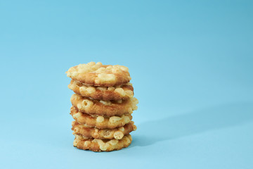 Cheese cookies are placed on top of each other, like a pyramid, isolated on light blue background. Nutritious snack.